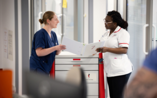 A colleague in scrubs discussing work with a colleague in NHS uniform